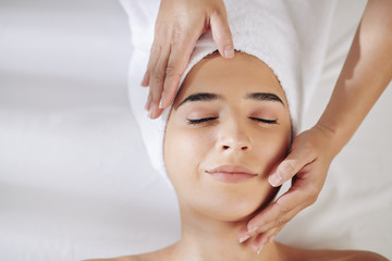 Beautiful smiling young woman enjoying rejuvenating face massage in beauty salon
