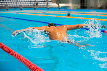Athletic man swimming in butterfly style in the swimming pool with clear blue water.