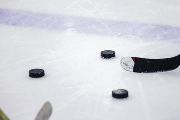 three ice hockey pucks on ice arena rink with two hockey sticks.