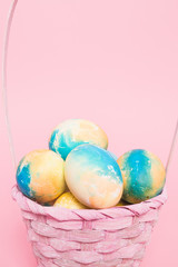 Multi-colored Easter eggs in a basket on a pink isolated background. Easter is a bright holiday.