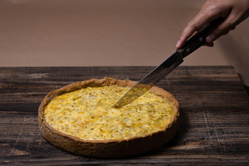 Hand with a knife cuts kish with caramelized onions, dill and cream cheese on a Wooden Table