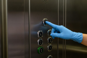 Inside the elevator. Female hand wants to press the elevator button in a protective blue glove. Antibacterial protection. Quarantine. The concept of self-isolation during a pandemic and epidemic.