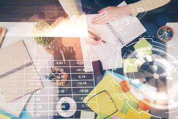 Hand taking notes in notepad. Forex chart holograms in front. Concept of research. Double exposure