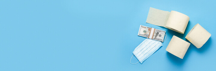 toilet paper rolls, medical mask and dollars banknotes on a blue background. Baner. Flat lay, top view. Concept hygiene product, virus, deficiency, quarantine