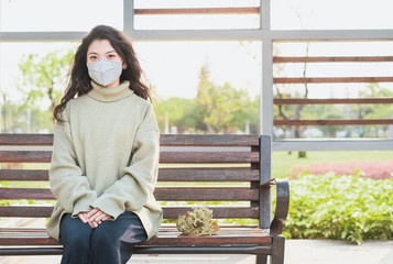 The long-haired girl wearing a mask sitting on a park bench