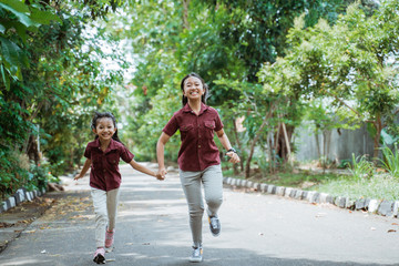 asian sisters running outdoors holding hands and smiling on the street in park