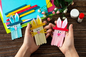Child is holding Easter bunny toy gift stics puppets on wooden table. Handmade. Project of...
