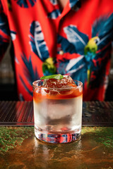 A tiki style colourful layered cocktail in a rocks glass with crystal clear ice cube, garnished...