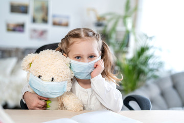 little girl in a mask , hugging a Teddy bear, looking sad, concept of e-learning