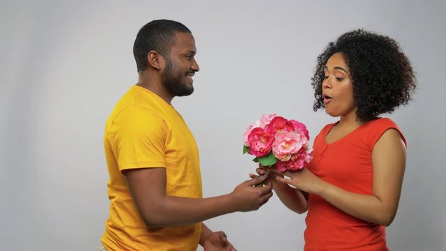 holiday, greeting and people concept - happy african american couple with bunch of flowers over grey background