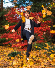 A young businessman in a session hitting the leaves of the autumn trees