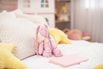 Fototapeta na wymiar Handmade plush rabbit made of fabric sits on a cozy bed in the children 's room.