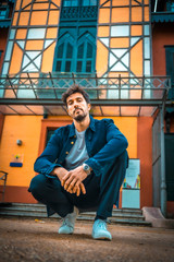 A young enterprising businessman crouched on the ground with an orange house in the background