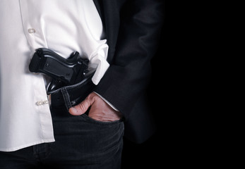 Man hides gun at his belt of jeans , on dark background  - 332369562