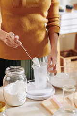 Cropped image of woman putting soda lye powder in plastic jar and measuring it on electronic scale...
