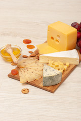 different types of cheese with nuts and dried apricots, grapes and honey on a wooden board. Top view