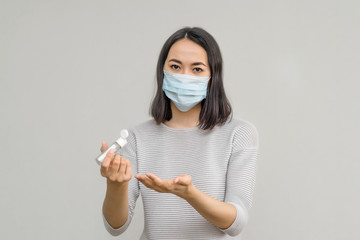 a young Asian woman in a medical mask and holding an antiseptic alcohol in her hands on a gray background. protection from the coronavirus and flu pandemic