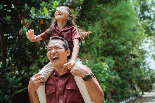 Cheerful father carrying on neck smiling daughter while walking in the park