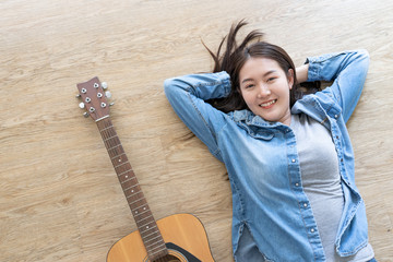 Asian young woman music lover relax and happy sleeping lie down on oak wooden floor with guitar  from flat lay top view