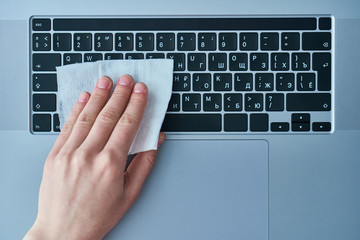 Office worker disinfects and cleans the working keyboard with antibacterial wet wipes to protect...