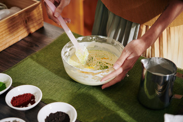 Close-up image of woman using plastic spatula when mixing melted soap with powder colorants