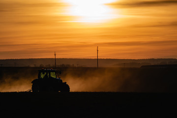 Fototapeta premium Tractor silhouette in the field on the orange-yellow sunset