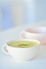 Homemade matcha latte on a white table, a light pink cup on the background, matcha green tea latte in a white cup with copy space. Matcha is a powder of green tea leaves and a delicious energy booster