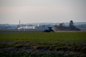 Fototapeta premium Tractor silhouette in the field on the orange-yellow sunset