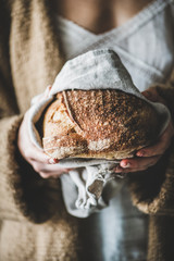 Woman holding freshly baked healthy rye Swedish bread round loaf in hands, selective focus
