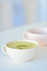 Homemade matcha latte on a white table, a light pink cup on the background, matcha green tea latte in a white cup with copy space. Matcha is a powder of green tea leaves and a delicious energy booster