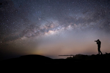 Milky way night panorama with silhuettes of a man intent on photographing the night sky.