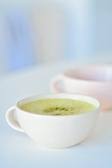 Homemade matcha latte on a white table, a light pink cup on the background, matcha green tea latte in a white cup with copy space. Matcha is a powder of green tea leaves and a delicious energy booster