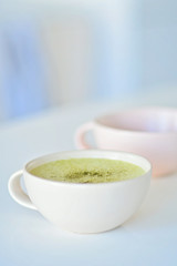 Homemade matcha latte on a white table, a light pink cup on the background, matcha green tea latte in a white cup with copy space. Matcha is a powder of green tea leaves and a delicious energy booster