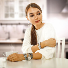 Young woman in nostalgic mood sitting in her bright atmospheric kitchen at white wooden table. Copy...