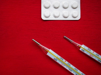 Top view of two thermometers and white pills on a red background. Virus, pandemic, medicine