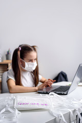 Distance learning online education. schoolgirl in medical mask studying at home, working at laptop notebook and doing school homework. coronavirus quarantine.