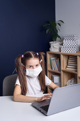 Distance learning online education. a schoolgirl in medical mask studying at home, working at laptop notebook and doing school homework. coronavirus quarantine.