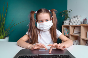 Distance learning online education. schoolgirl in medical mask studying at home, working at laptop notebook and doing school homework. covid quarantine concepte.