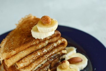 Closeup stacked pancakes with nuts and banana and liquid golden honey. On a blue plate and a light gray background