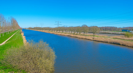 Canal separating a rural and an urban residential area below a blue sky in sunlight in spring