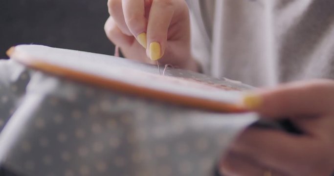 Unrecognizable woman embroidering beautiful bunny. 4k close up macro shot of female hands sewing cross-stitch.