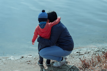 A woman with her son looks at the water in the lake. Mother and son are hugging near the lake