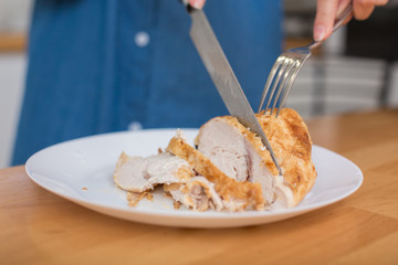Girl in blue jeans shirt slicing grilled chicken fillet for caesar salad at home kitchen