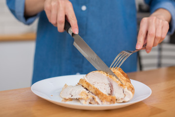 Girl in blue jeans shirt slicing grilled chicken fillet for caesar salad at home kitchen