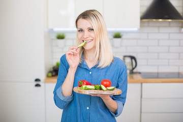 Girl in a blue denim shirt holds in hands plate with fresh vegetables (bell pepper, cucumber, tomato). Vegetarian food concept.