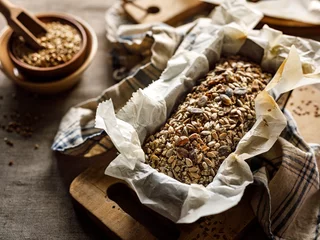 Fototapeten Brot Glutenfreies hausgemachtes Buchweizenbrot mit Zusatz verschiedener Samen in einer Backform auf einem Holzbrett aus nächster Nähe  © pbd Studio