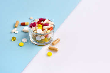 A glass full of pills, tablets, capsules on blue and white background
