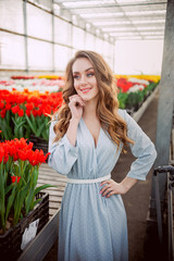 Beautiful woman in long wavy hair in a greenhouse with red tulips. Blue polka dot dress.