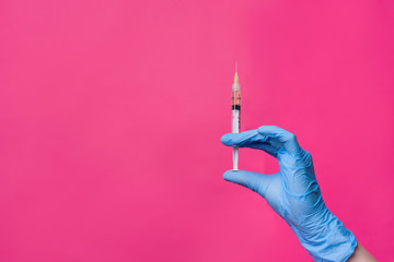 Close-up of a hand with a syringe on a pink background, concept of health, cosmetology, treatment...