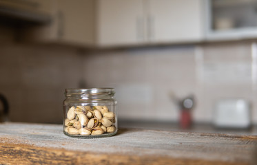 Pistachios in a jar which standing on a white vintage table with a kitchen on background. Pistachio is a healthy vegetarian protein nutritious food. Pistachios on rustic old wood.